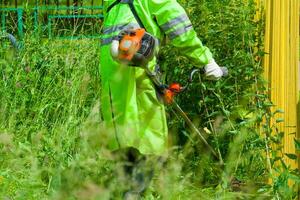 une homme tond le grand herbe avec une tondeuse photo