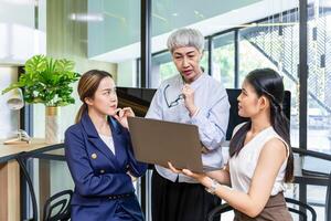 Sénior femme d'affaires équipe chef est guidage Jeune membre à affaires Succès par montrant information dans portable ordinateur pour objectif réussite pour Commencez et la créativité projet photo