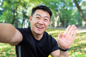 asiatique sportif coureur dans l'automne parc à la recherche à téléphone intelligent caméra et souriant, parlant avec copains sur appel, homme dans tenue de sport pour aptitude dans l'automne forêt. photo