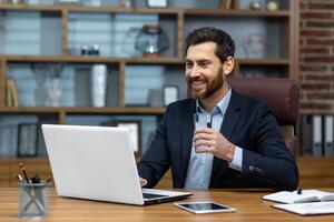 réussi mature homme à lieu de travail à l'intérieur Bureau travail à table avec portable en portant verre de nettoyer l'eau dans mains patron en buvant l'eau content fonctionnement. photo