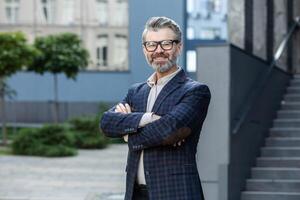 professionnel Sénior homme dans affaires tenue souriant en toute confiance en plein air, avec Bureau toile de fond, dépeindre succès. photo