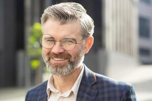 expérimenté Sénior homme avec une chaud sourire permanent en toute confiance à l'extérieur un bureau, habillé dans une professionnel affaires costume. photo