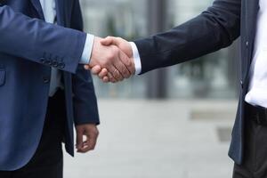 fermer photo, deux les hommes d'affaires saluer chaque autre et secouer mains, collègues de à l'extérieur le Bureau bâtiment confirmer le accord dans affaires costume photo