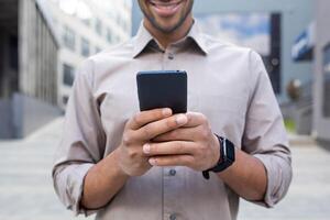 proche en haut de homme mains, homme d'affaire dans chemise en portant téléphone, en utilisant app sur téléphone intelligent, en marchant dans ville à l'extérieur Bureau bâtiment. photo