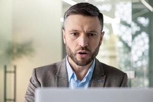 une professionnel homme d'affaire concentrés profondément tandis que travail sur le sien portable dans une bien éclairé, contemporain Bureau environnement. il apparaît absorbé et sérieux. photo