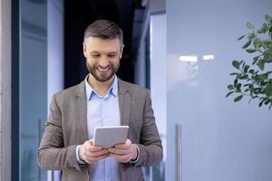 mature expérimenté homme d'affaire à l'intérieur Bureau souriant avec contentement, Sénior homme en portant tablette ordinateur dans mains, patron dans affaires costume en utilisant analytique financier application. photo