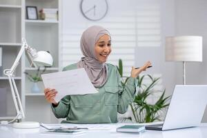 de bonne humeur musulman femme d'affaires engageant dans une appel avec clients, mettant en valeur sa les documents avec une sourire dans une élégant, bien éclairé bureau. photo