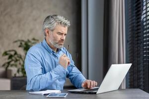 une mature professionnel est se concentrer sur le sien travail dans un bureau, en utilisant une portable et à la recherche pensif et concentré photo