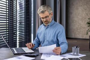 mature réussi financier comptable travail avec les documents papiers à l'intérieur le bureau, Sénior aux cheveux gris homme en pensant et sérieux à propos papier travail, homme d'affaire vérification rapports et contrats. photo