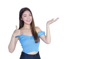 Jeune magnifique asiatique femme dans une bleu chemise est agissant pouce en haut comme une bien symbole et un autre main spectacles comme en présentant quelque chose tandis que isolé blanc Contexte. photo