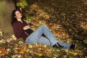 Jeune femme en train de dormir en dessous de une arbre dans l'automne photo
