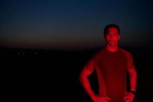 athlète grèves une pose en dessous de rouge la nuit lueur après intense toute la journée marathon. photo