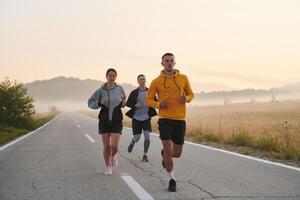 une groupe de amis, les athlètes, et joggeurs embrasse le de bonne heure Matin heures comme elles ou ils courir par le brumeux aube, excité par le en hausse Soleil et entouré par le tranquille beauté de la nature photo