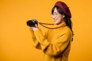 habillé dans une Jaune chandail et rouge béret, une Jeune asiatique femme artistiquement manie sa caméra comme elle poursuit sa passion pour la photographie et Voyage. photo