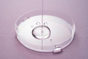 sérum ou cosmétique pétrole les flux dans une transparent bol sur une violet Contexte. photo