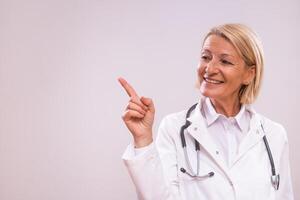 portrait de mature femelle médecin montrer du doigt sur gris Contexte. photo