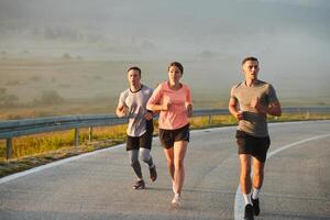 une groupe de amis, les athlètes, et joggeurs embrasse le de bonne heure Matin heures comme elles ou ils courir par le brumeux aube, excité par le en hausse Soleil et entouré par le tranquille beauté de la nature photo