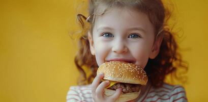 peu fille en mangeant Hamburger sur Jaune Contexte photo