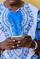 africain américain adolescent dans traditionnel soudanais tenue engagé avec téléphone intelligent photo