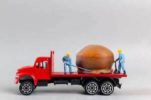 miniature ouvrier équipe en mouvement Chocolat Balle de un camion sur une gris arrière-plan, monde Chocolat journée concept photo