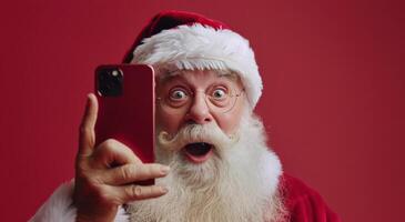 Père Noël claus à la recherche à téléphone intelligent avec surpris expression contre rouge Contexte photo