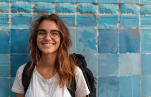 Jeune femme avec sac à dos sourit tandis que permanent dans de face de bleu tuile mur photo