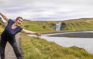 en voyageant femme ayant amusement dans de face de le célèbre Skogafoss waterfal photo