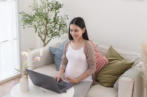 Enceinte femme travail sur portable et intelligent téléphone dans le vivant pièce à Accueil photo