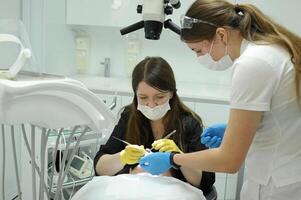 fermer médical dentiste procédure de les dents nettoyage le médecin et le infirmière courbé plus de le patient, elles ou ils traiter le dents, elles ou ils remplir le canaux photo