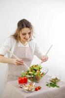 Jeune magnifique adolescent fille remue avec diligence salade elle penché plus de bol peu souriant vert salade feuilles nappe de table beige Couleur restaurant nourriture cuisine spectacle délicieux petit déjeuner salade pour le déjeuner photo