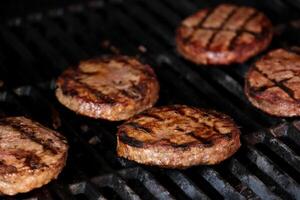 hamburgers cuisine sur barbecue gril avec flammes sur une gril sont moitié frit haché Boulettes de viande pour une fait maison Burger Contexte pour un barbecue dans le été avec charbon et Frais Boulettes de viande photo