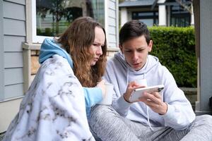 mal nouvelles adolescent garçon et fille Regardez à le téléphone dans mécontentement montrer du doigt enveloppé dans une couverture résoudre problèmes social réseaux l'Internet la communication avec copains se plaindre souffrir photo