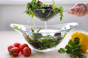 une femme chef dans une rayé tablier est est déchirure fraîchement lavé, frais, nettoyer feuilles de salade dans une séparé verre bol. elle est situé dans une rustique style cuisine. photo