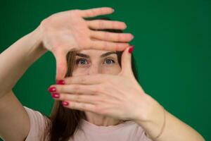 magnifique fille encadrement sa visage avec sa mains différent émotions de une Jeune fille sur une vert Contexte chromakey magnifique faciale Caractéristiques réel gens rose T-shirt blanc écorché. européen photo