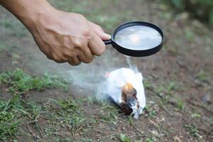 proche en haut main tenir grossissant verre à faire Feu pour brûlant papier. concept, science expérience à propos convexe lentille, tenir grossissant verre entre le Soleil et Tinder. pratique survie compétences. photo