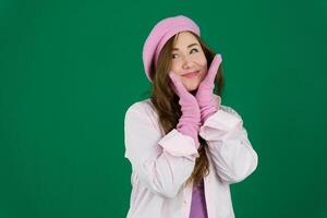 charmant fille portant rose français chapeau. Jeune fille femme avec une rose béret sur sa tête France mode sur une vert Contexte chromakey. différent émotions rose veste gants longue marron cheveux. rose hiver photo