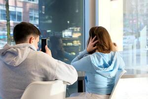 Jeune couple séance à café et en utilisant mobile téléphone de bonne humeur homme et femme sont séance dans café sortir ensemble bavarder du repos photo