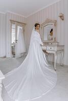 une la mariée est permanent dans de face de une miroir dans une pièce avec une blanc robe photo