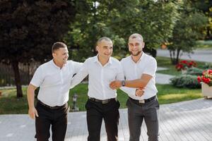 Trois Hommes dans blanc chemises et noir un pantalon sont permanent ensemble photo