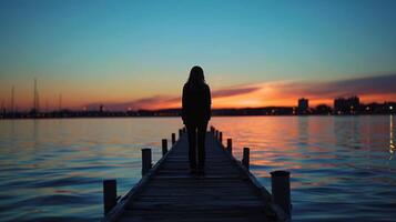 silhouette contre une le coucher du soleil ciel une la personne des stands sur une front de mer Dock avec retour à le caméra. le calme des eaux et serein couleurs . photo