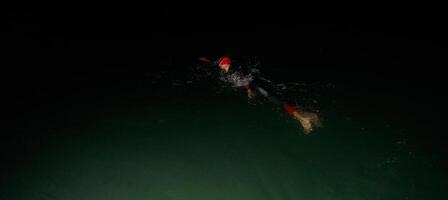 une déterminé professionnel triathlète subit rigoureux nuit temps formation dans du froid des eaux, mettant en valeur dévouement et résistance dans préparation pour un A venir triathlon nager compétition photo