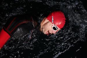 une déterminé professionnel triathlète subit rigoureux nuit temps formation dans du froid des eaux, mettant en valeur dévouement et résistance dans préparation pour un A venir triathlon nager compétition photo