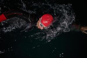 une déterminé professionnel triathlète subit rigoureux nuit temps formation dans du froid des eaux, mettant en valeur dévouement et résistance dans préparation pour un A venir triathlon nager compétition photo