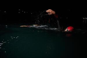 une déterminé professionnel triathlète subit rigoureux nuit temps formation dans du froid des eaux, mettant en valeur dévouement et résistance dans préparation pour un A venir triathlon nager compétition photo