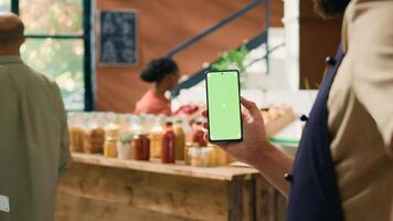 local vendeur détient téléphone intelligent app avec écran vert afficher, en présentant fond La technologie sur mobile appareil. Jeune homme montrant isolé maquette écran à épicerie boutique vérifier. photo