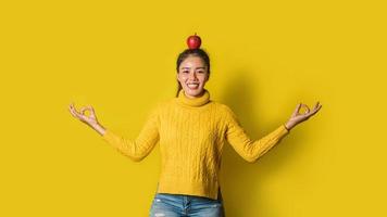 joyeuse jeune femme sur fond jaune en studio. une fille avec une pomme posée sur la tête tout en faisant du yoga. le concept d'exercice pour une bonne santé. amoureux de la santé
