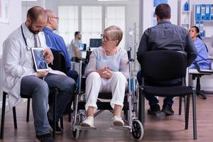 Docteur homme assis dans la zone d'attente de l'hôpital avec une femme handicapée senior photo