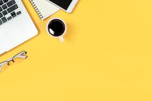 table d'espace de travail avec ordinateur portable, fournitures de bureau, tasse à café, téléphone portable et tasse à café sur fond jaune