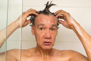 homme mûr prenant une douche et se lavant les cheveux avec du shampoing