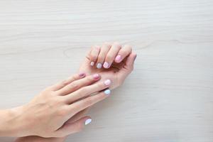 manucure féminine pastel élégante et tendance en blanc, rose et bleu. les mains de la belle jeune femme sur fond en bois. copiez la bannière de l'espace photo